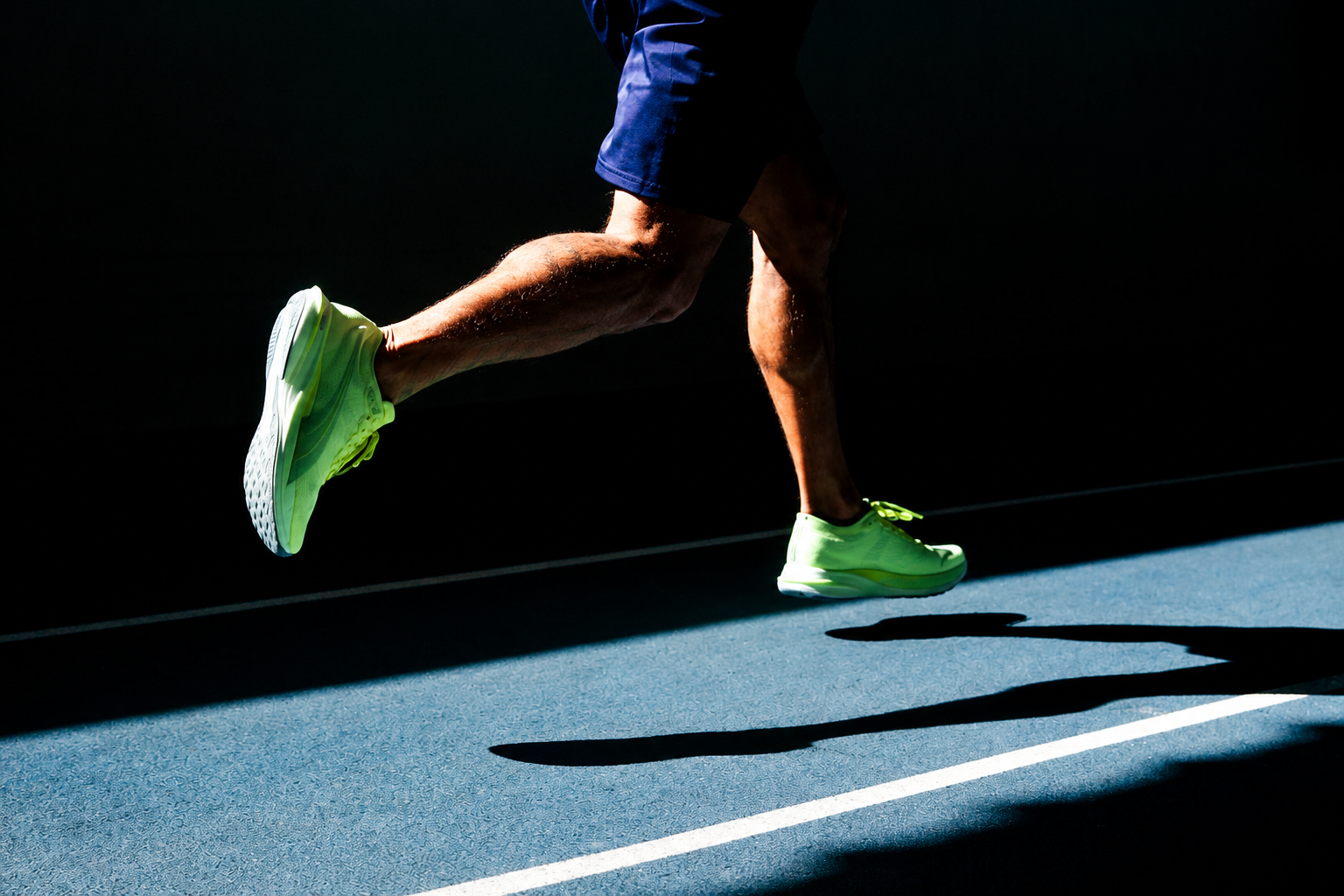 Runner on a track, neon shoes, dark surface.
